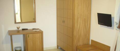 Una habitación con un escritorio de madera, un espejo, un armario, un banco y un televisor.