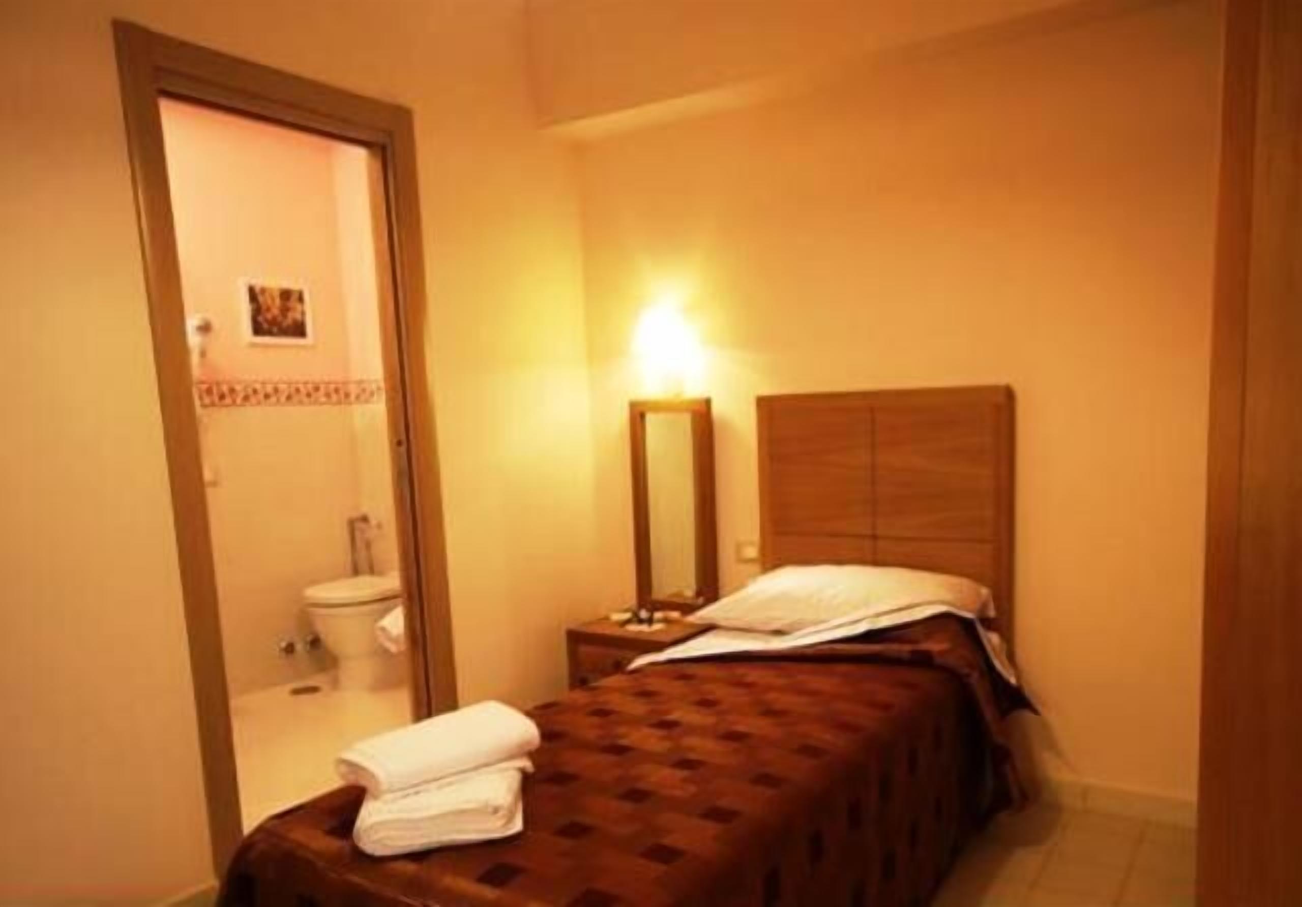 Un dormitorio pequeño y acogedor con una cama individual, una mesita de noche con lámpara y un cabecero de madera.