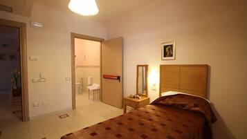 Quarto de hotel com cama, mesa de cabeceira e porta para um banheiro.