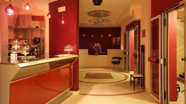 A modern hotel lobby with a red and beige color scheme, a reception desk, a seating area, and a decorative ceiling light fixture. - Palace Hotel Una Nuova Strada (Nocera Terinese)