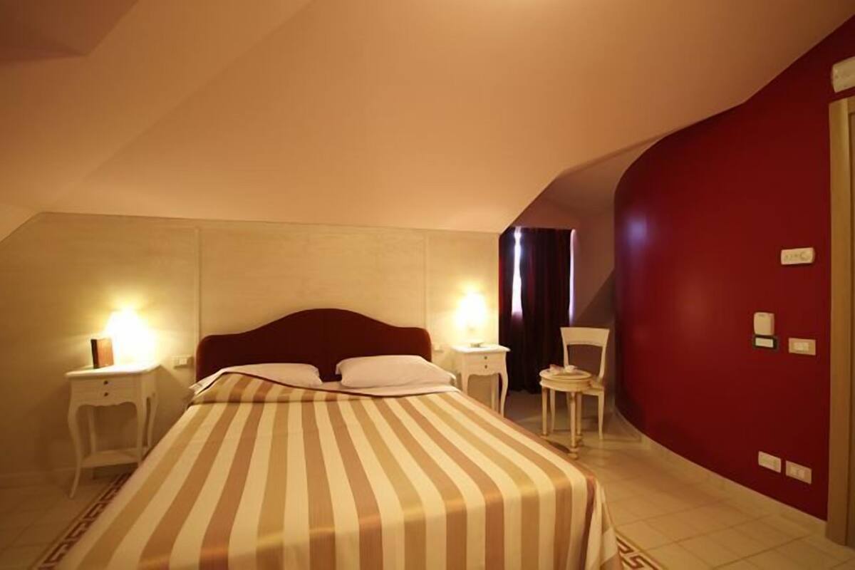 A hotel room with a bed, bedside tables, a chair, and a red wall.