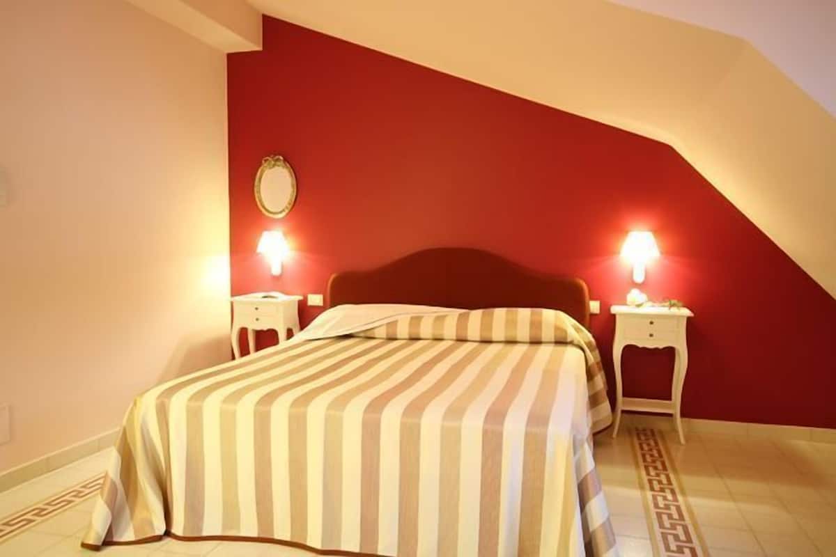 A bedroom with a bed, two bedside tables, and a red accent wall.
