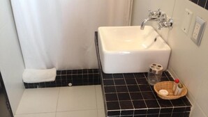 A bathroom with a white sink, black tiled floor, a towel, and a basket with toiletries.