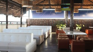 Restaurante com assentos brancos e castanhos, paredes de bambu e luminárias pendentes.