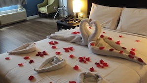 Quarto de hotel com uma cama bem arrumada, uma luminária, uma cadeira e um telefone em uma mesinha de cabeceira.