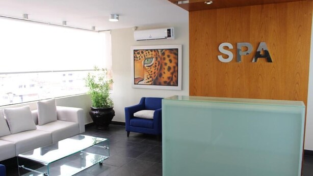 Uma área de recepção de spa moderna, com uma mesa de centro de vidro, uma poltrona azul e uma obra de arte com estampa de leopardo na parede.