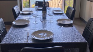 A dining table set with plates, wine glasses, and a bottle, overlooking a lake and mountains.