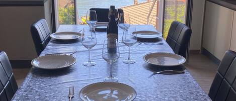 A dining table set with plates, wine glasses, and a bottle, overlooking a lake and mountains.