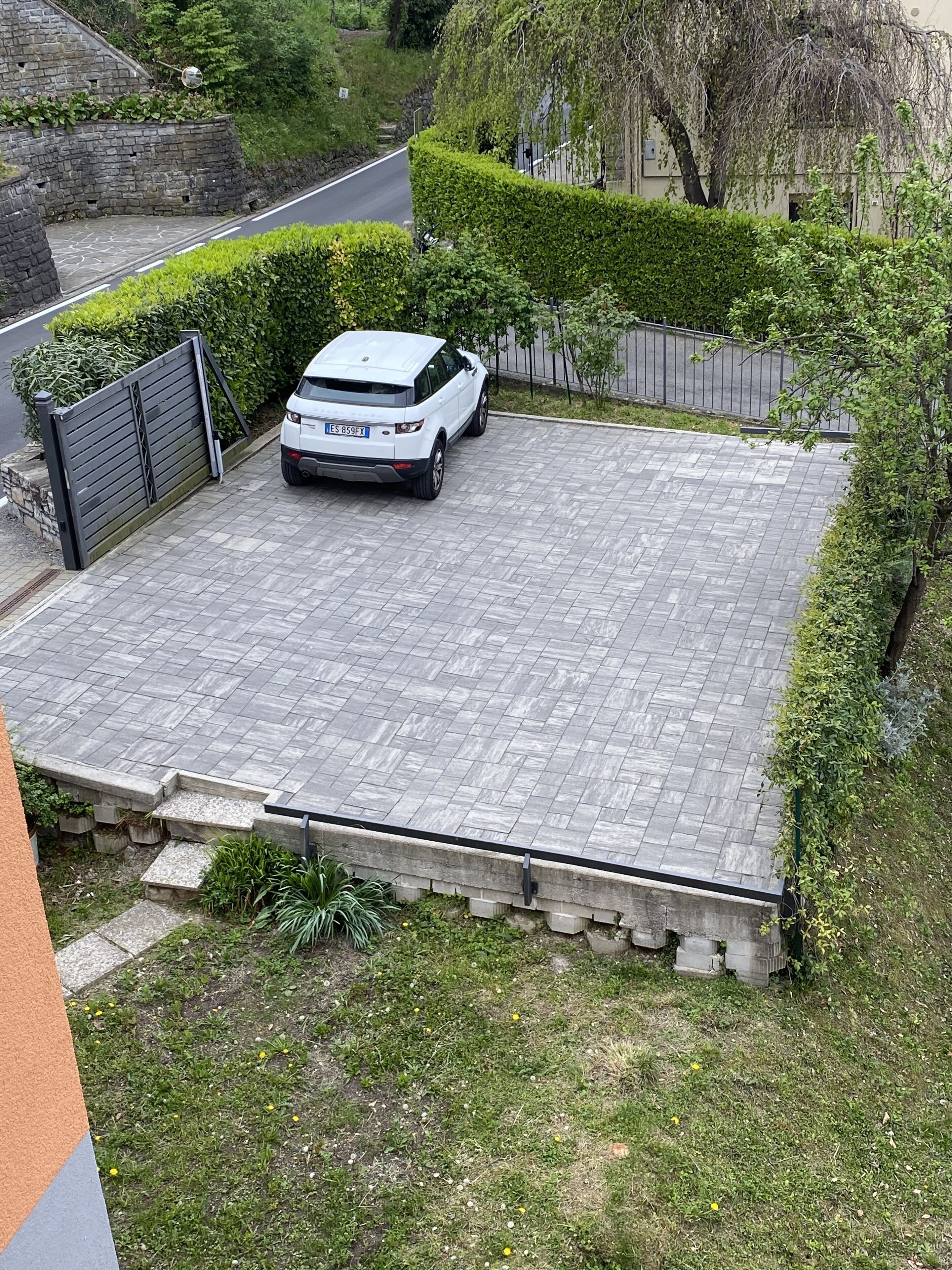 Ein gepflasterter Weg führt zu einem weißen SUV, das vor einer Grundstücksmauer mit einem Eingangstor parkt.