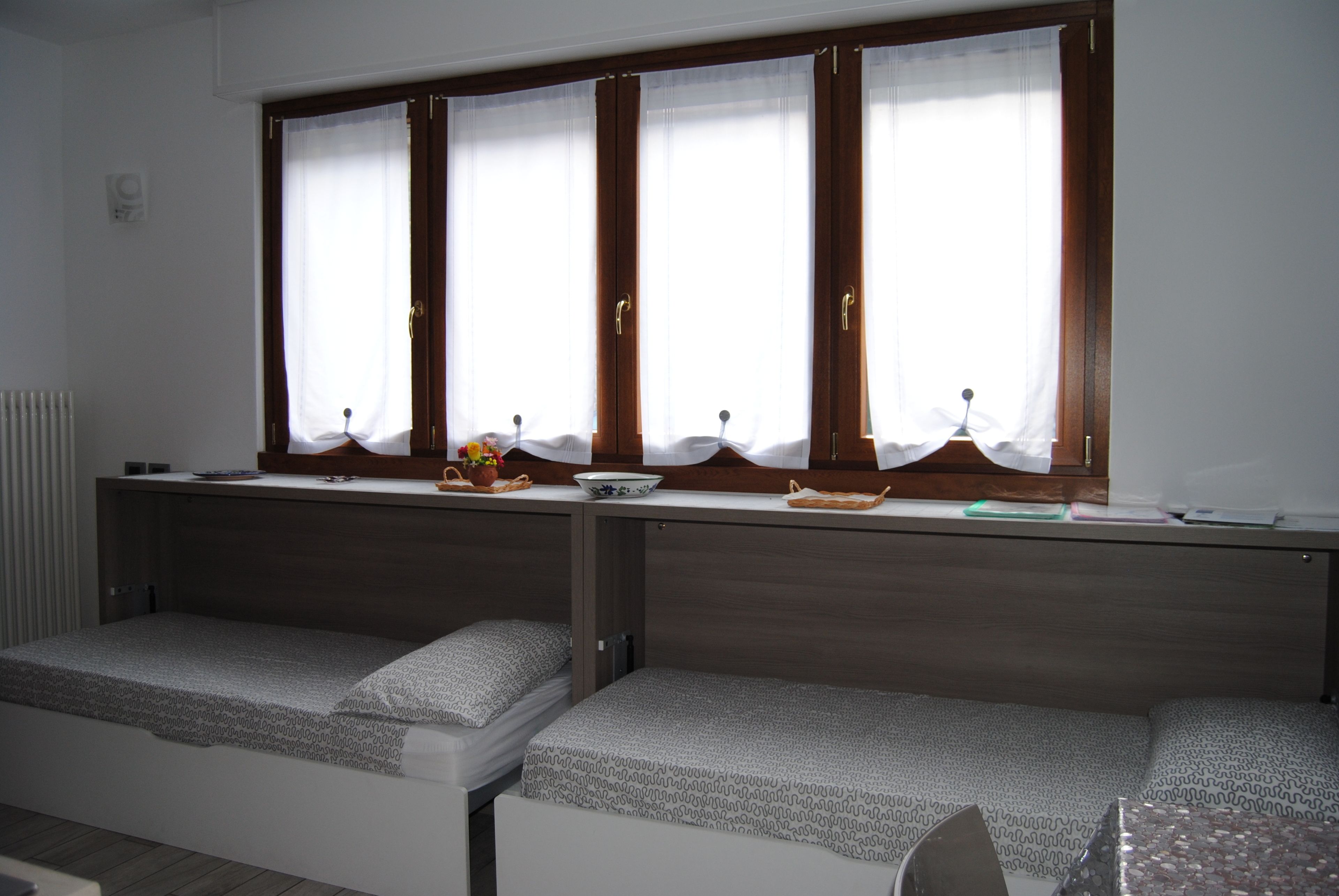 A room with a bed, a small table with a bowl and a plant, and a window with curtains.