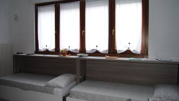 A room with a bed, a small table with a bowl and a plant, and a window with curtains.