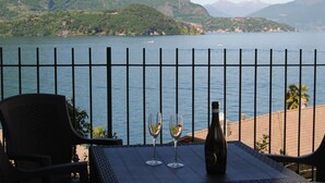 A table with two wine glasses and a bottle, overlooking a lake with mountains in the background.