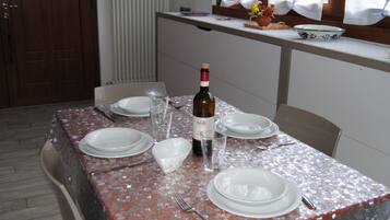 Ein Esstisch ist gedeckt mit Tellern, Besteck und einer Weinflasche, über dem Tisch ein Fenster und dahinter eine Heizung.