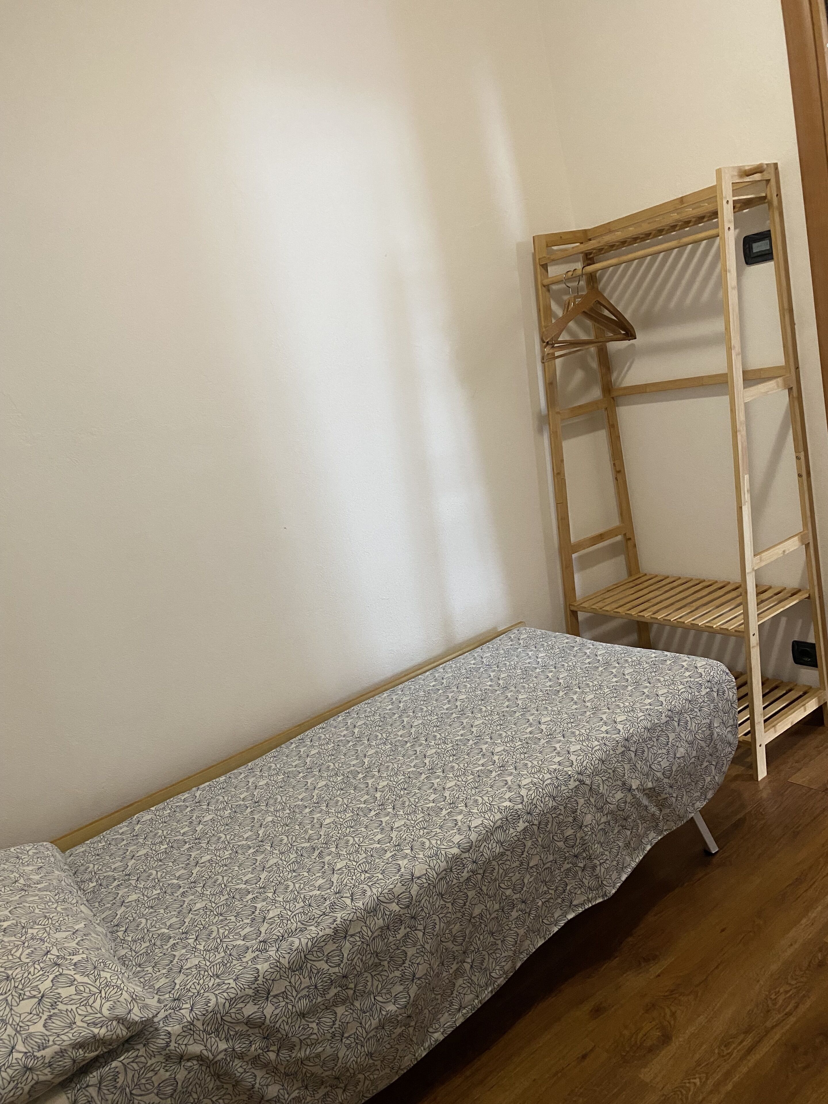 A small, single-bed room with a wooden bunk bed against the wall, a wooden floor, and a plain white wall.