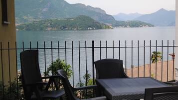 Uma varanda com duas cadeiras de vime e uma mesa, com vista para um lago e montanhas ao fundo.