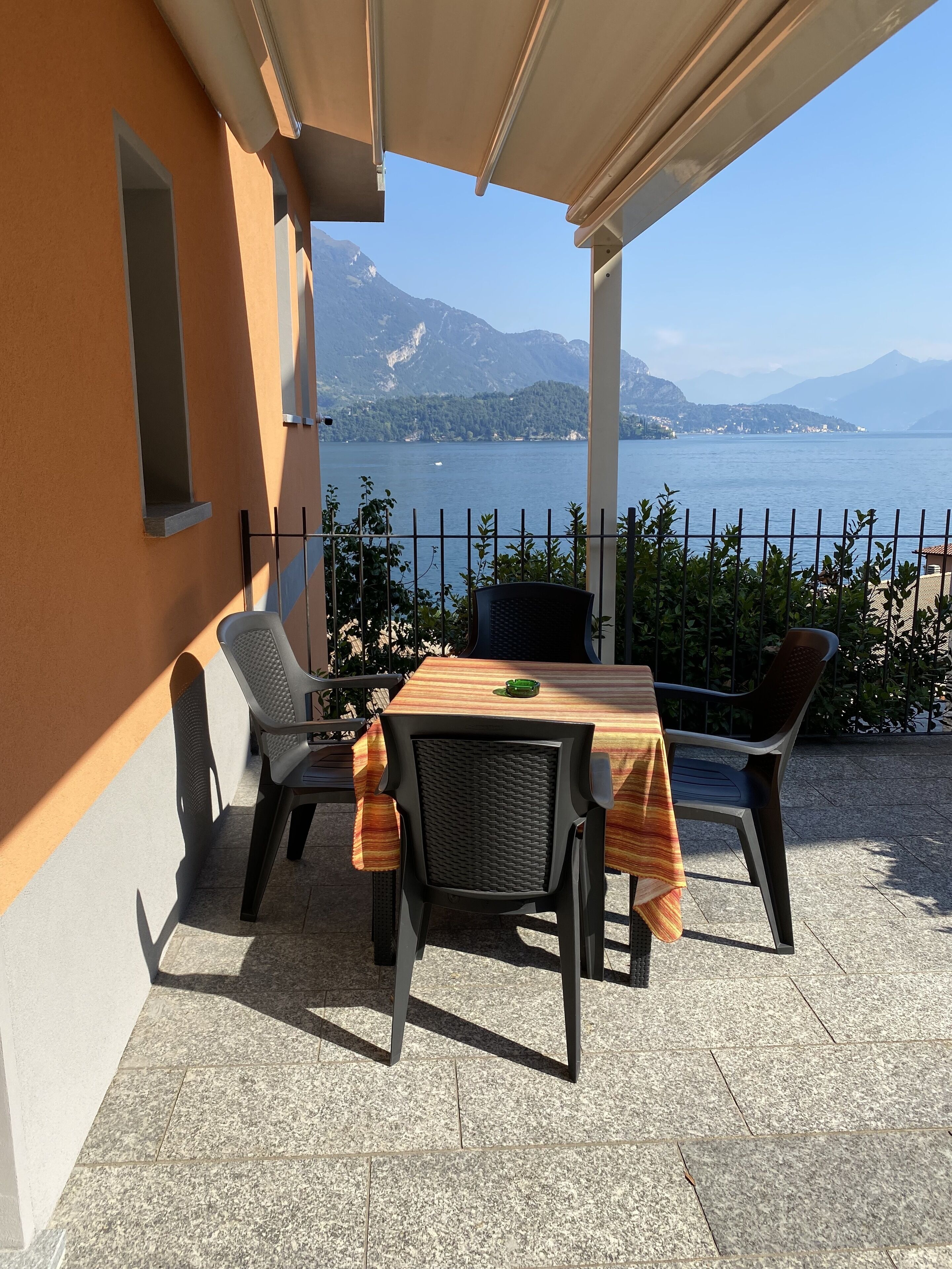An outdoor patio with a table and chairs, overlooking a lake with mountains in the background.