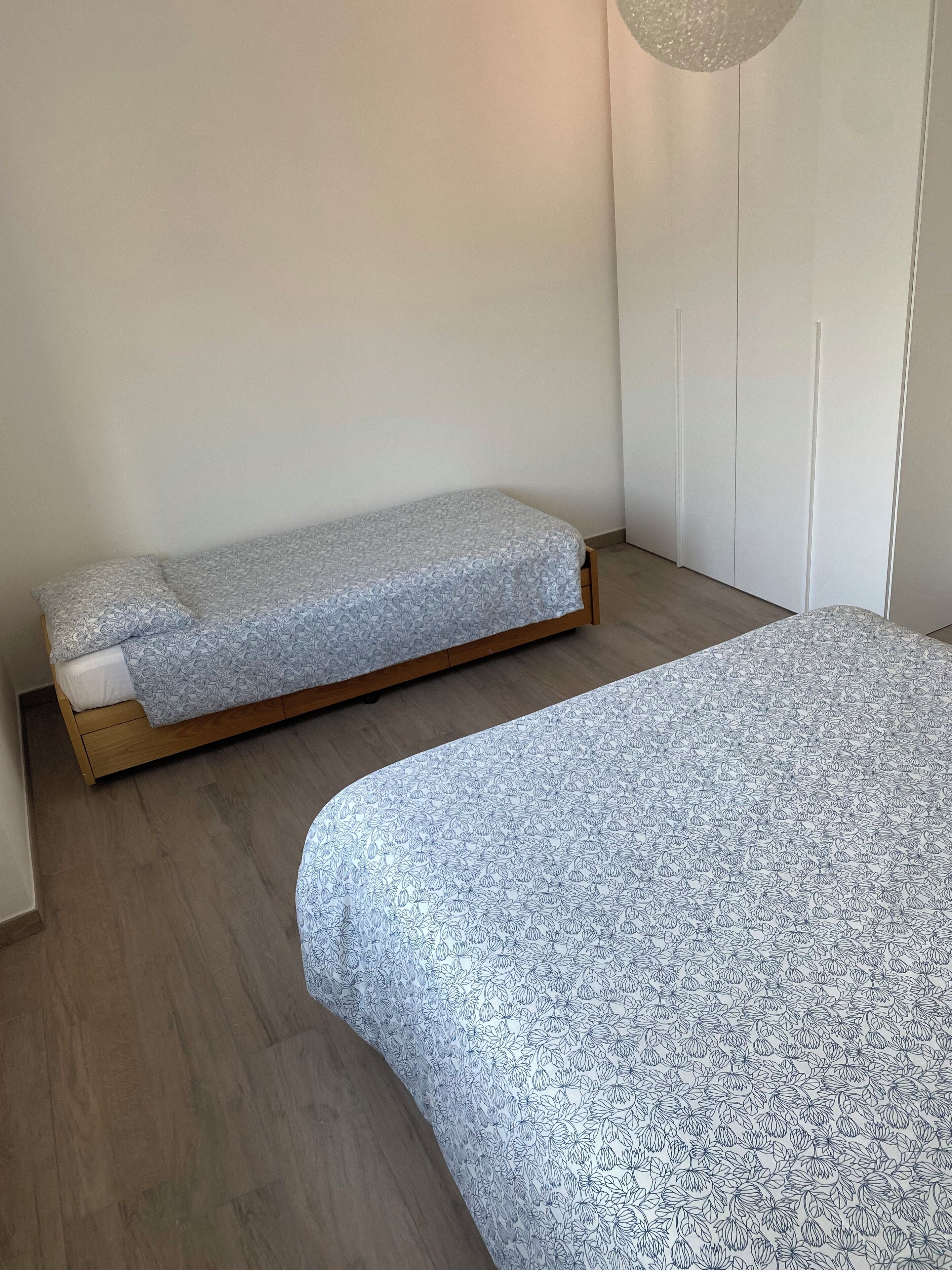 Un dormitorio con dos camas individuales, suelo de madera y un armario blanco.