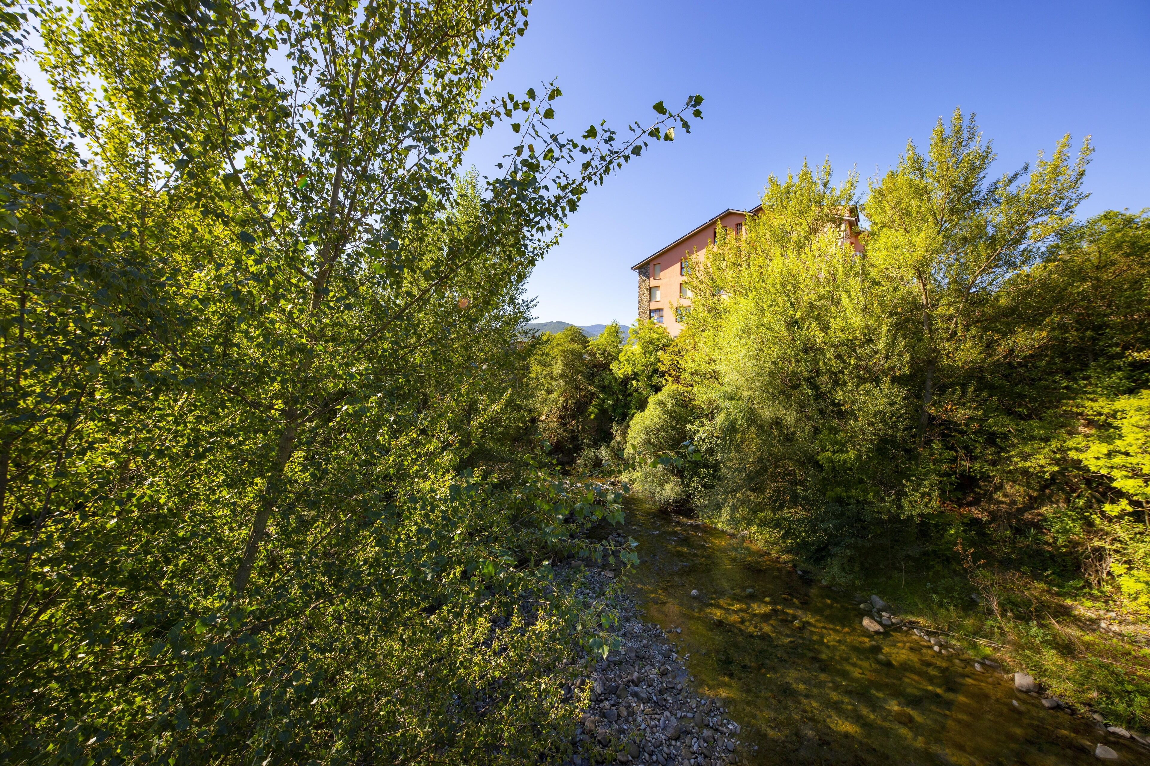 A river flowing through a wooded area with a building in the background.
