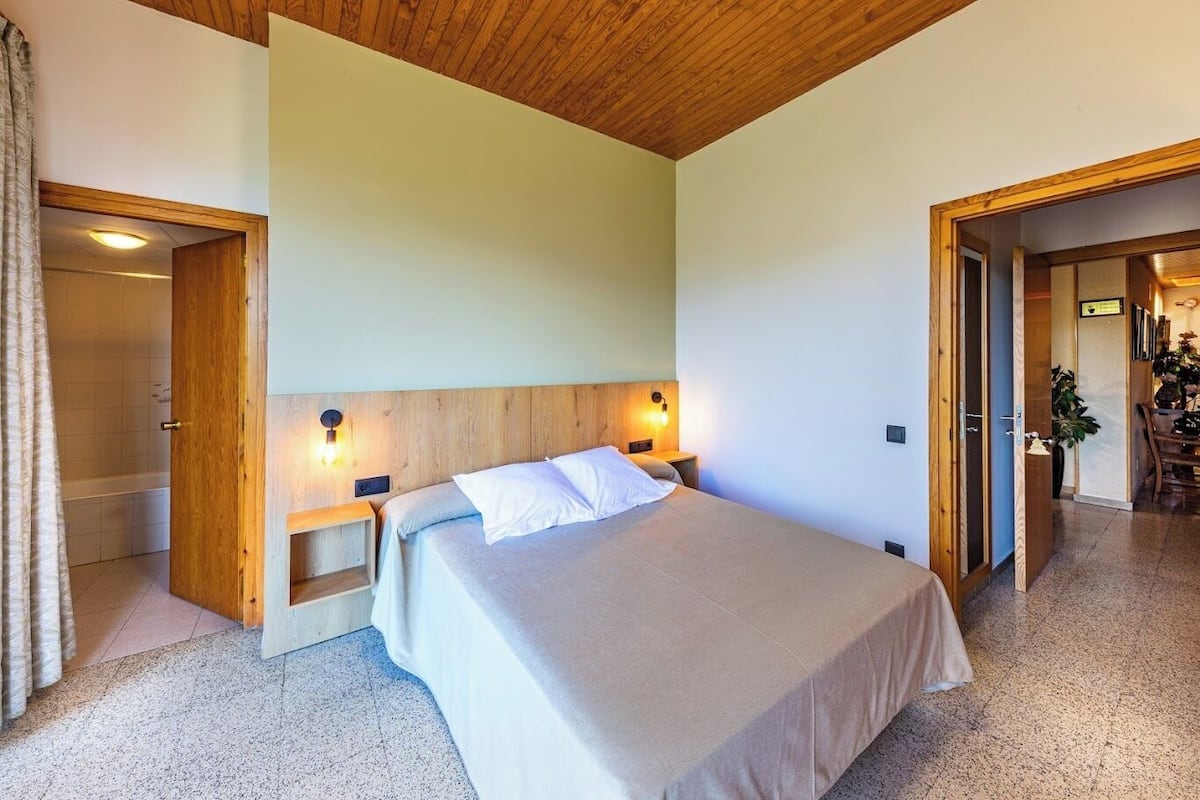 Un dormitorio con techo de madera, una cama con ropa de cama blanca, dos lámparas de noche y un mesita de noche de madera.