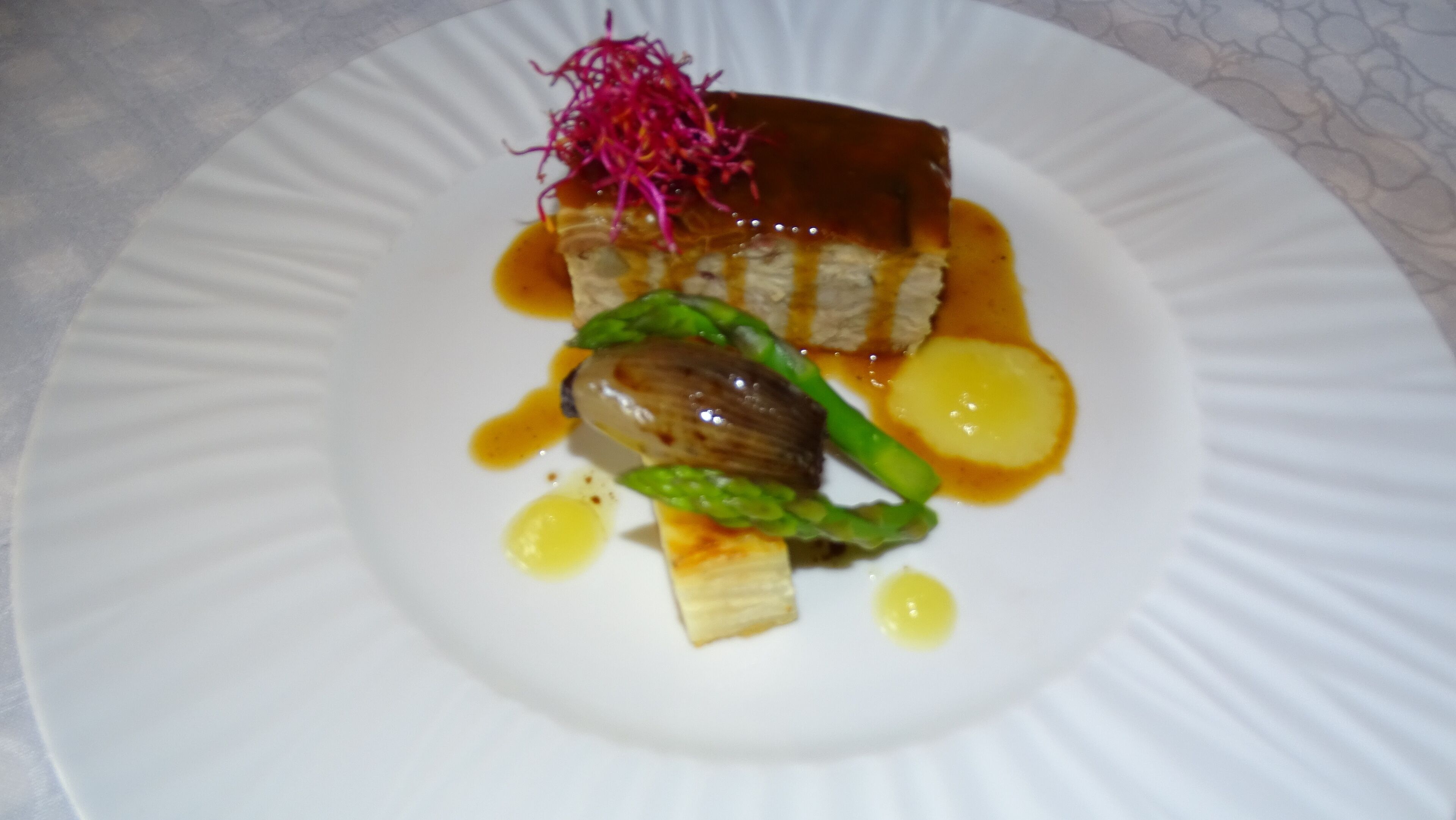 A plate with a piece of meat, green vegetables, and a garnish on a white plate.