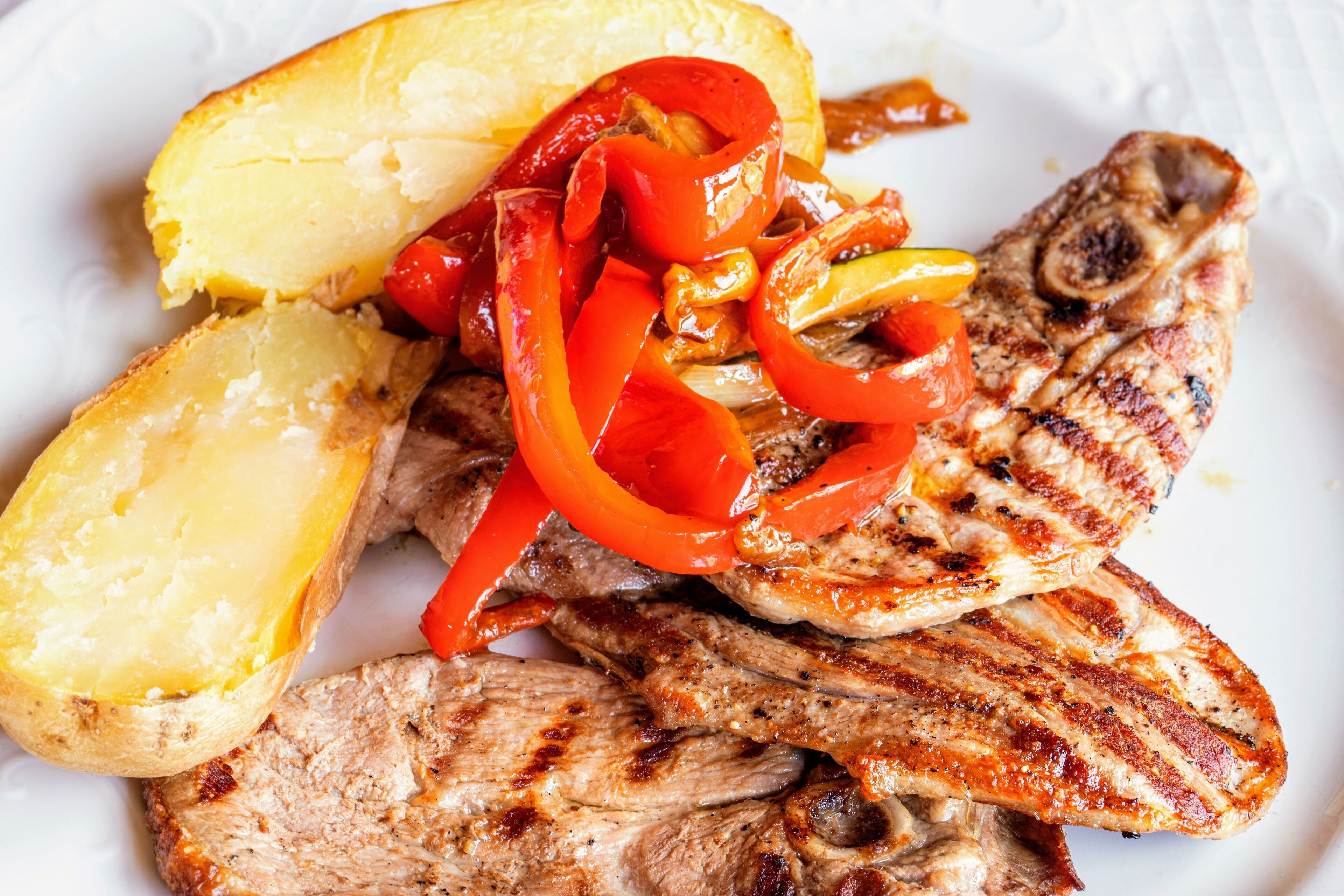 Une assiette de viande grillée, de pommes de terre en tranches et de poivrons grillés.