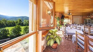 A dining area with wooden tables and chairs, a potted plant, and a view of the countryside.