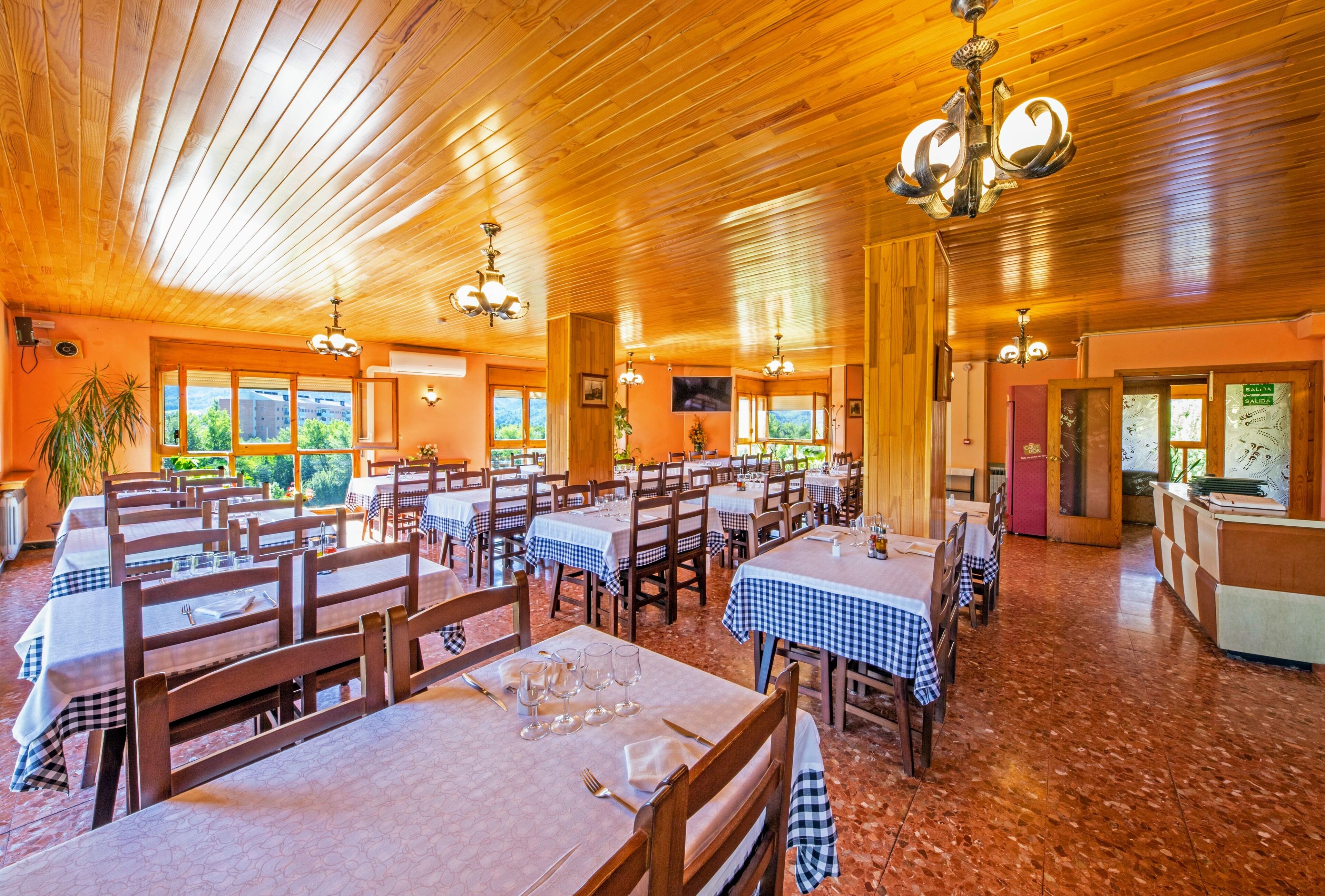 A restaurant with wooden ceiling and walls, checkered tablecloths, and multiple dining tables.