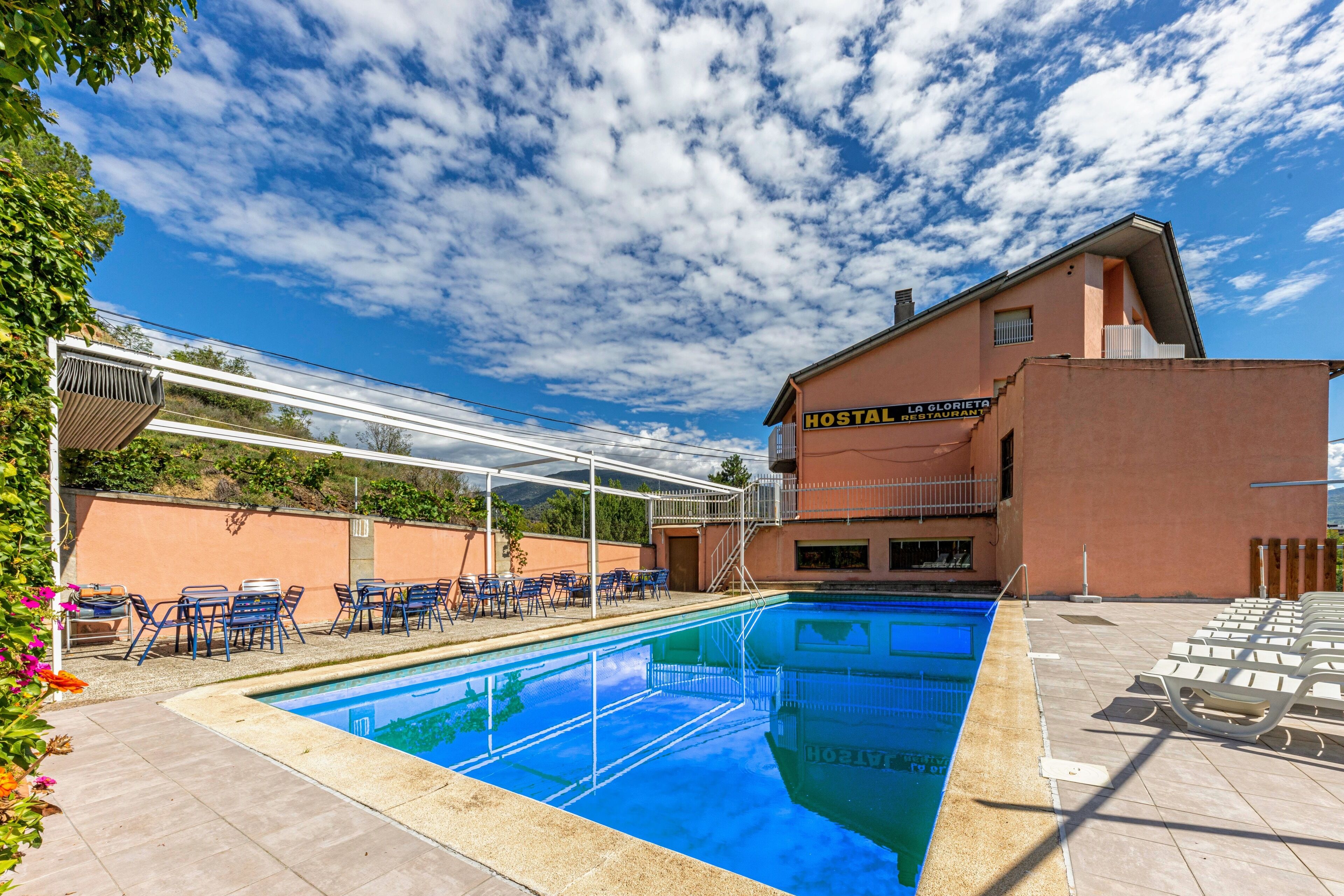 A swimming pool with lounge chairs and a covered area, adjacent to a building labeled "HOSTAL LA GLORIA RESTAURANT".