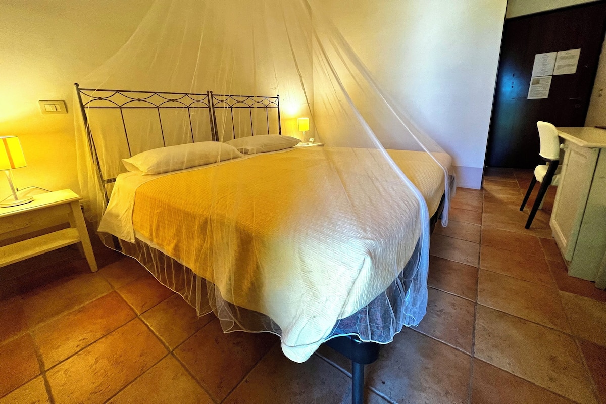 Ein Bett mit Baldachin, ein Nachttisch mit Lampe und ein Stuhl in einem Zimmer mit Fliesenboden.