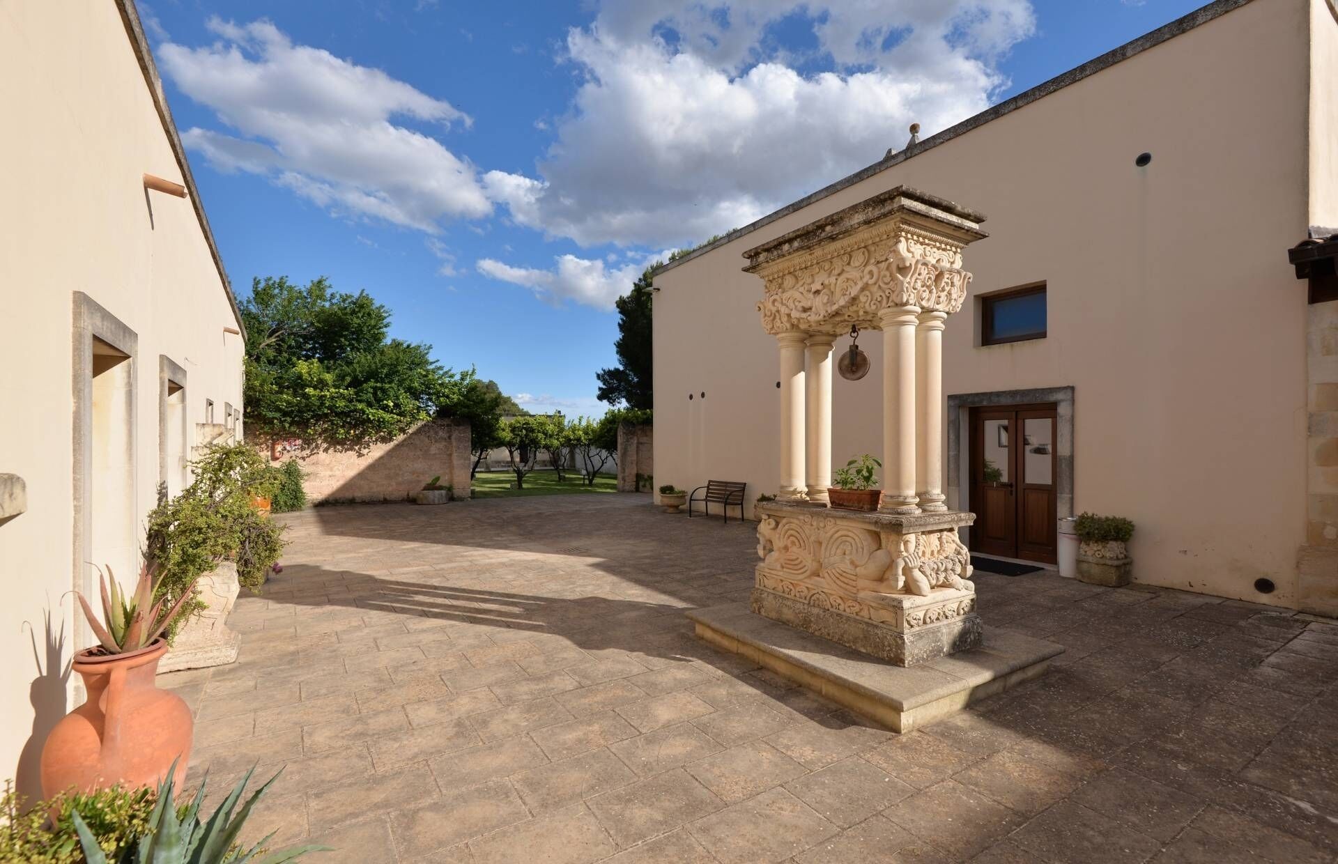 Un patio con una fuente de piedra en el centro, un banco y plantas en macetas.