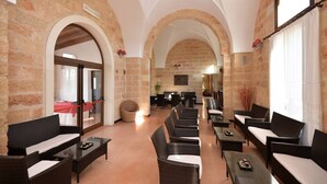 A spacious lobby with high arched ceilings, stone walls, and a central seating area with wicker furniture. - Masseria Li Campi (Cavallino)