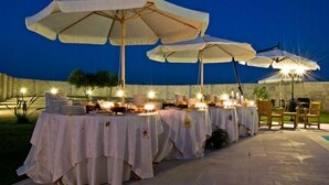 An outdoor dining area with tables set up under large umbrellas, each table adorned with candles and plates. - Masseria Li Campi (Cavallino)