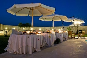 An outdoor dining area with tables set up under large umbrellas, each table adorned with candles and plates. - Masseria Li Campi (Cavallino)
