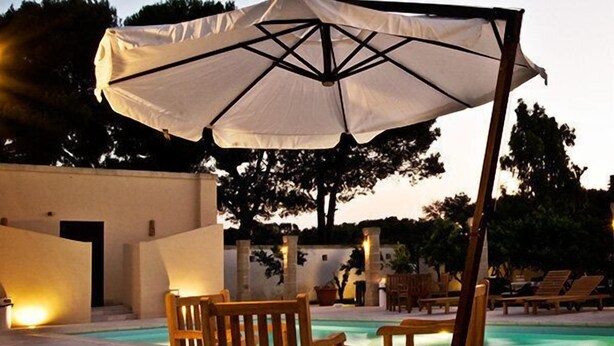 A poolside area with wooden chairs and a large umbrella. - Masseria Li Campi (Cavallino)