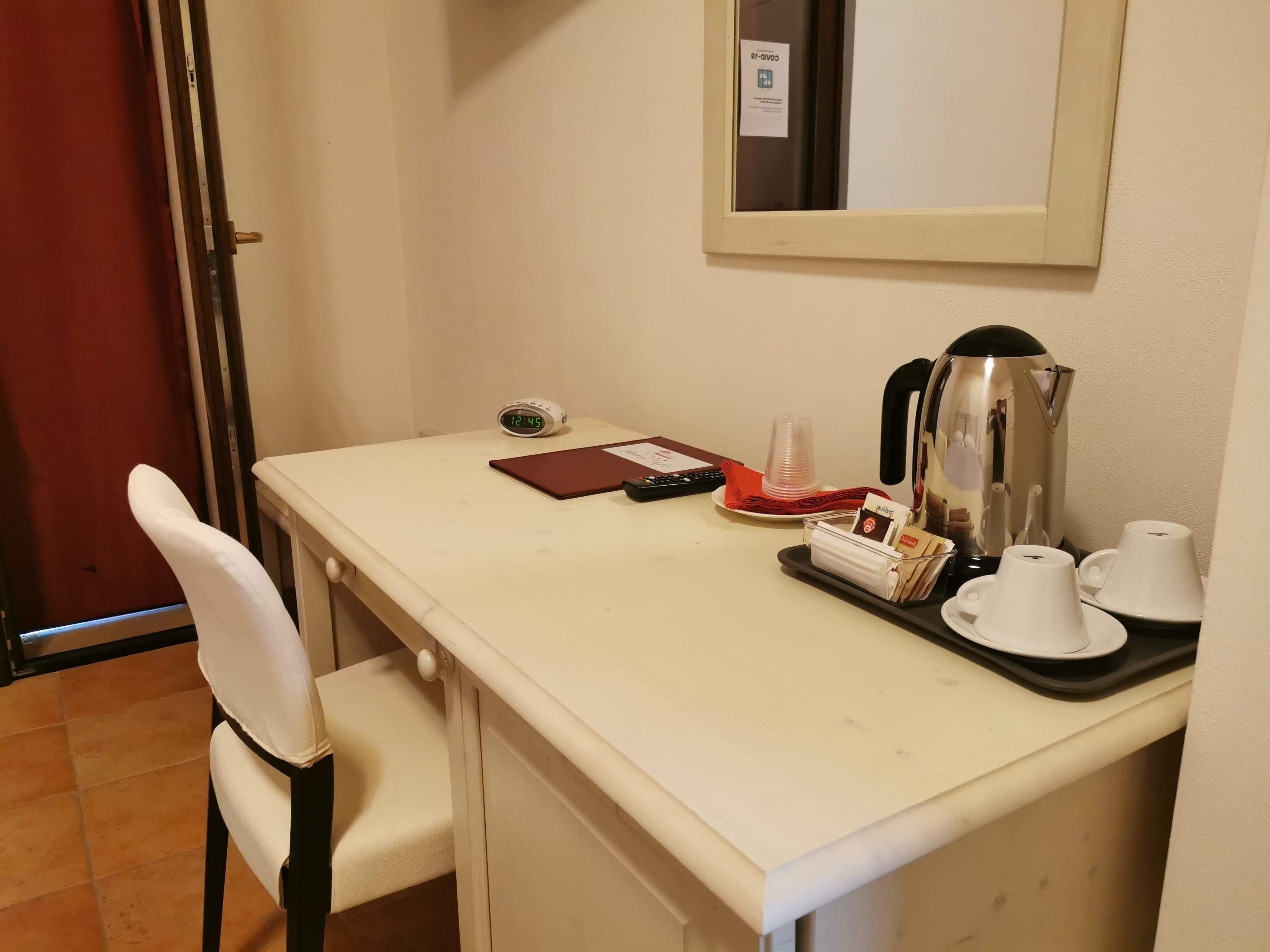 Habitación de hotel con escritorio, silla, reloj, tetera y bandeja con tazas y una libreta.