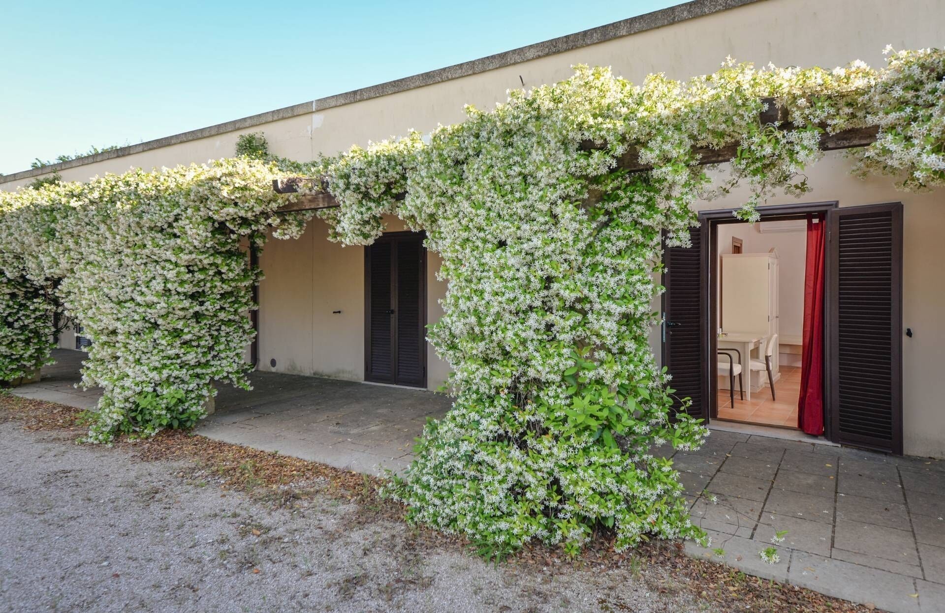 Um edifício com área externa coberta, apresentando uma série de arcos e uma porta com persianas.