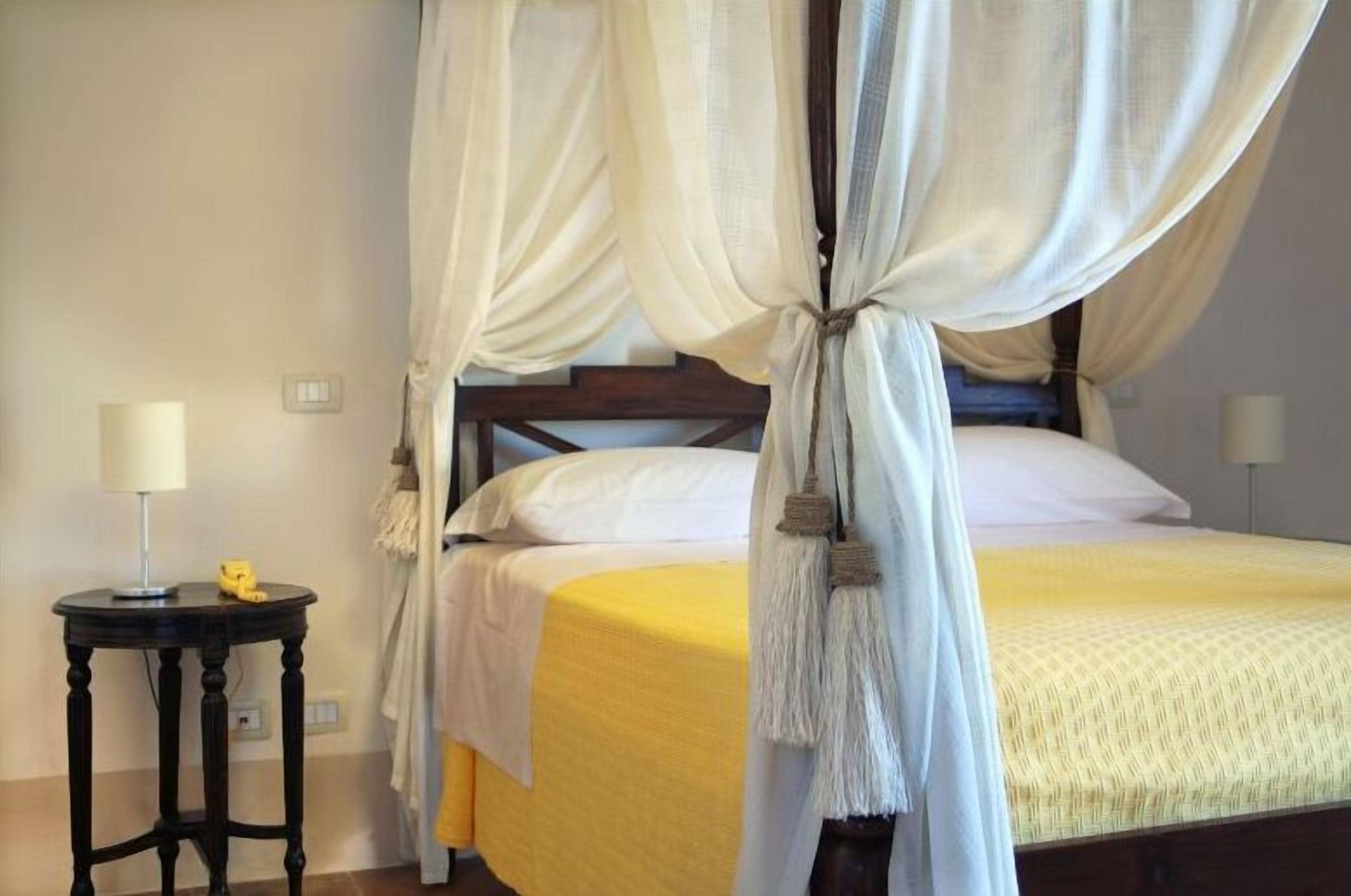 Une chambre à coucher avec un lit recouvert de draps jaunes, une table de chevet avec une lampe et un lit à baldaquin avec des rideaux blancs.