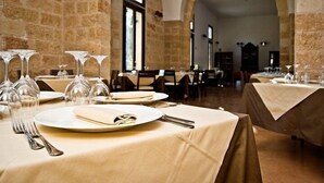 A dining area with tables set for a meal, featuring clear glassware and plates, in a room with stone walls and an arched doorway. - Masseria Li Campi (Cavallino)