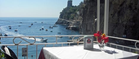 A table with a white tablecloth and a sign, overlooking a coastal area with boats and cliffs.
