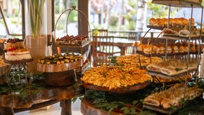 A buffet with various food items displayed on tiered stands and a cake on a wooden stand. - Ocaporã Hotel - All Inclusive (Ipojuca)