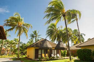 Un resort con estructuras de techo de paja, palmeras y un cielo azul claro.