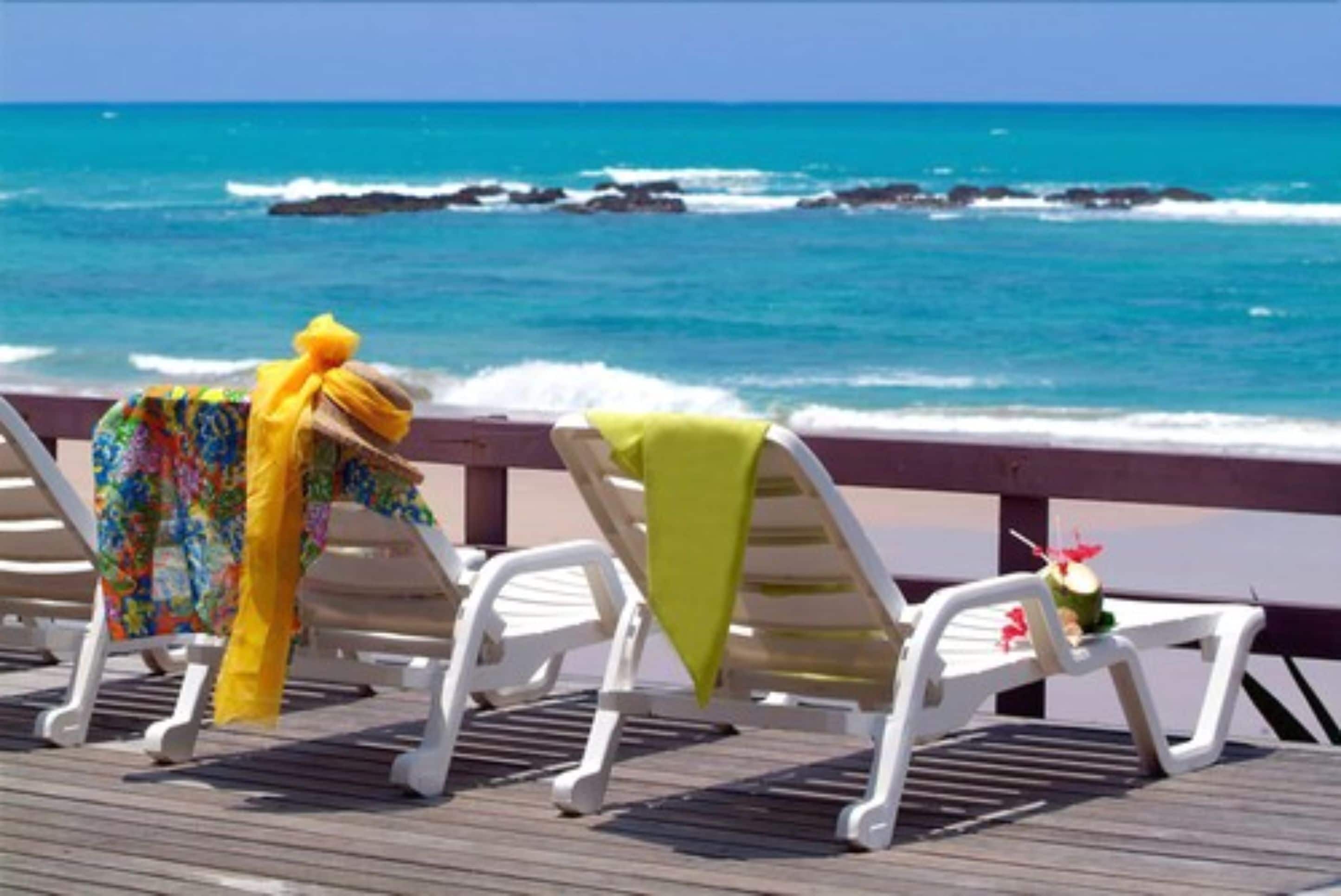 A beachside deck with lounge chairs and a table, overlooking the ocean.
