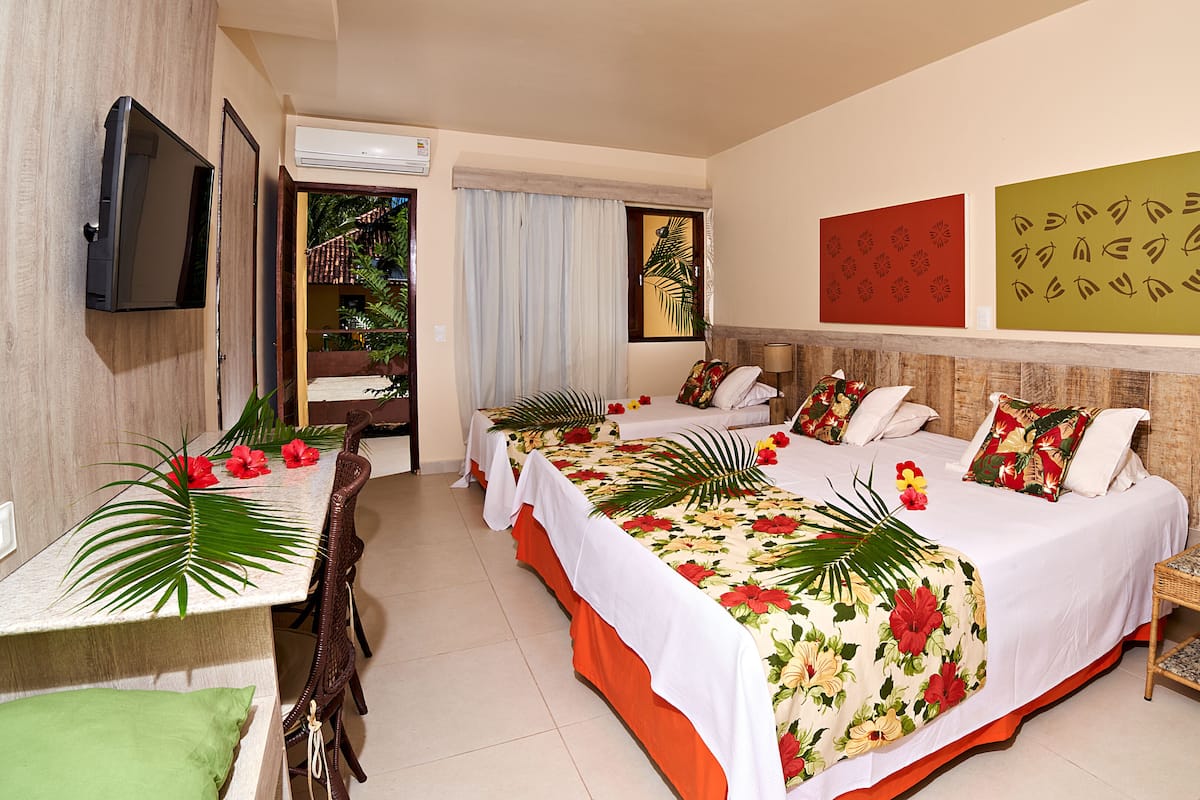 A hotel room with a large bed, two smaller beds, a dining table, and a TV.