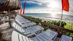 A beachside lounge with white lounge chairs and a thatched-roof structure. - Ocaporã Hotel - All Inclusive (Ipojuca)