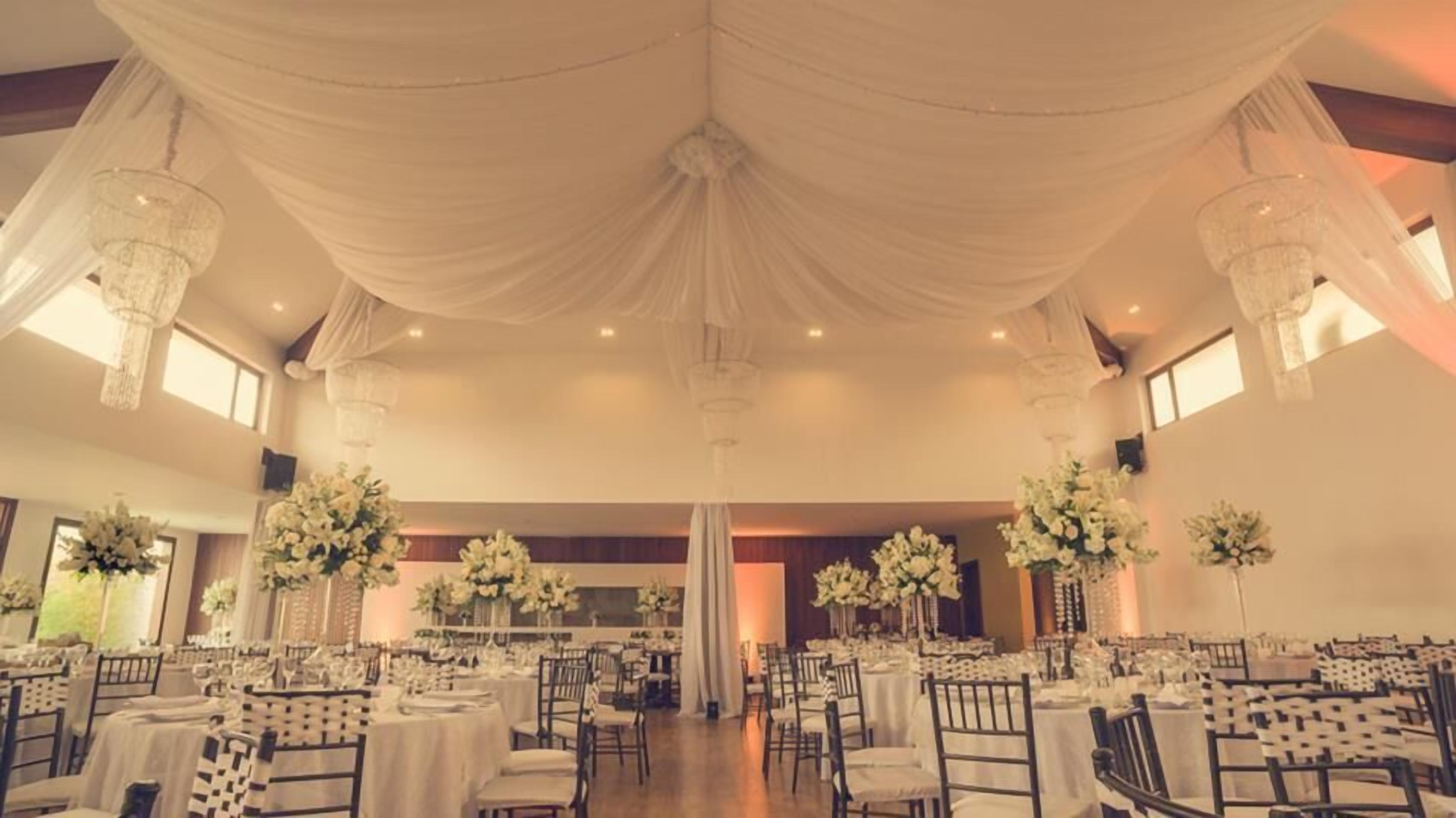 A banquet hall with round tables, chandeliers, and floral centerpieces.