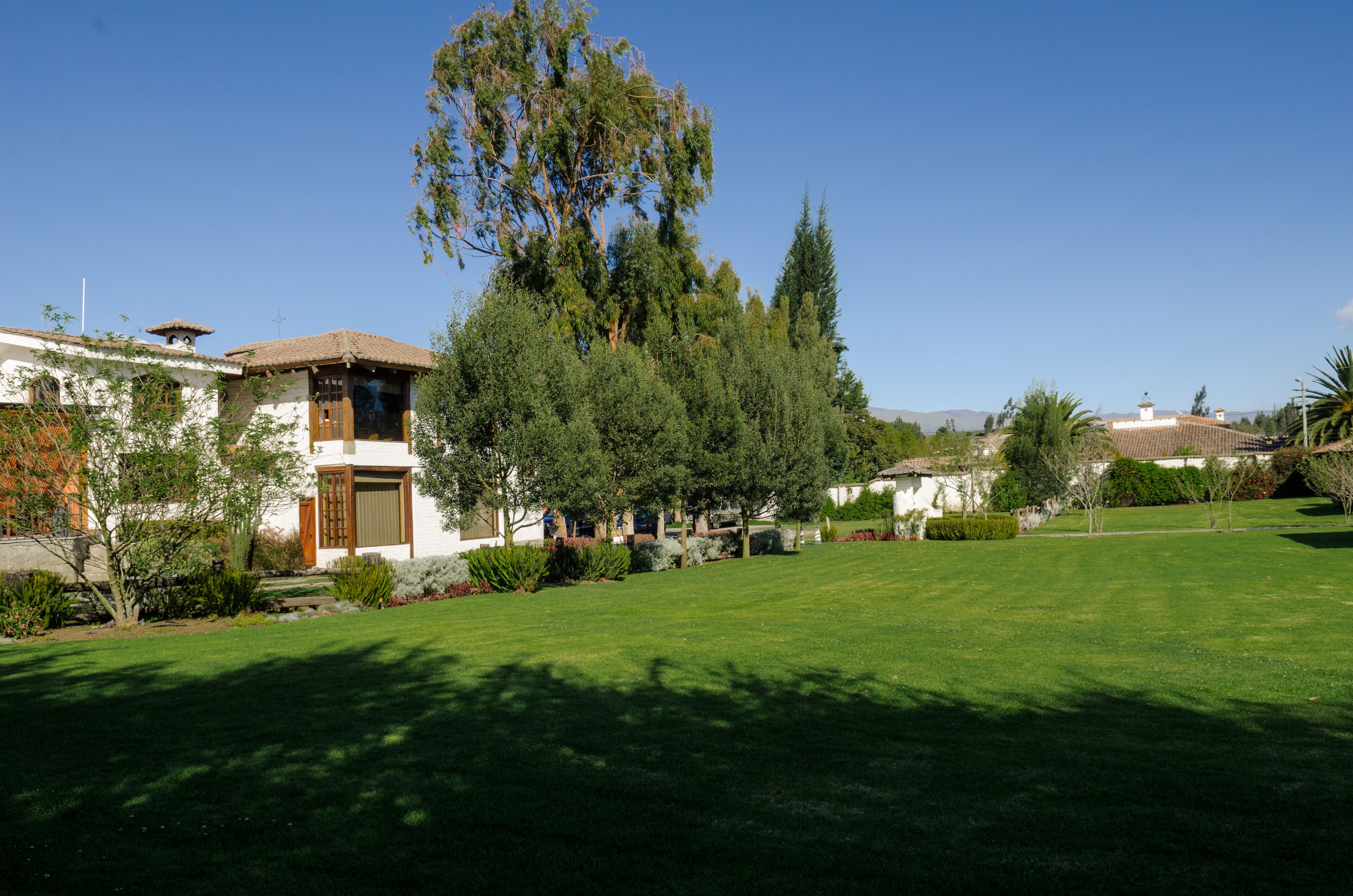 A residential property with a well-maintained lawn, mature trees, and a two-story house with a tiled roof.