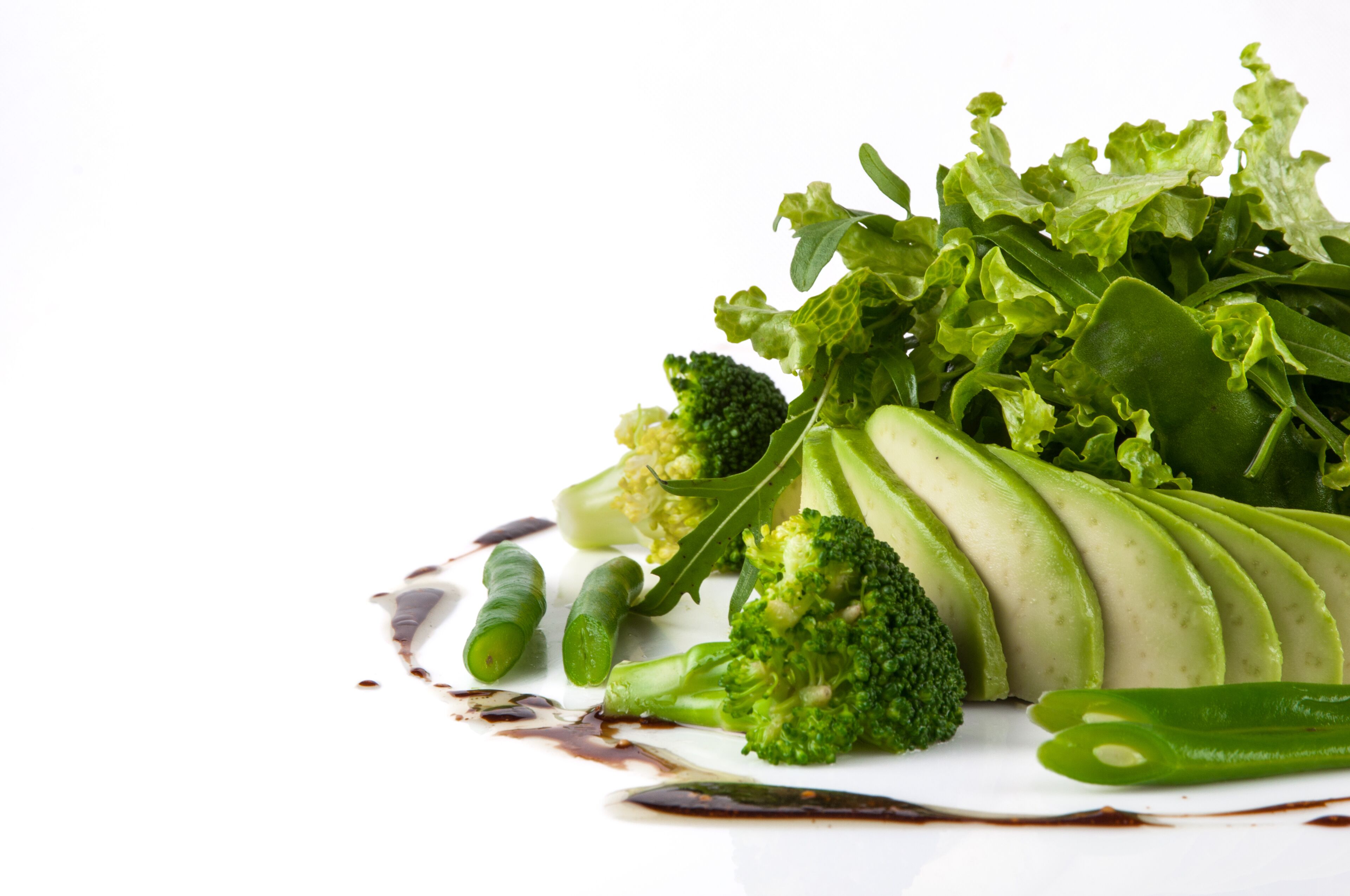 Variedad de verduras frescas, como brócoli, judías verdes y hojas verdes, dispuestas sobre un plato blanco con salsa oscura.