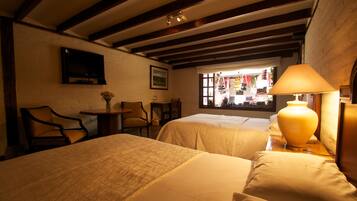 A hotel room with two beds, a TV mounted on the wall, a window with a view of the street, and a lamp on the nightstand.