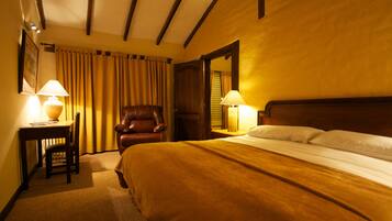 A hotel room with a large bed, two bedside lamps, a wooden headboard, a leather armchair, and a wooden desk with a lamp.