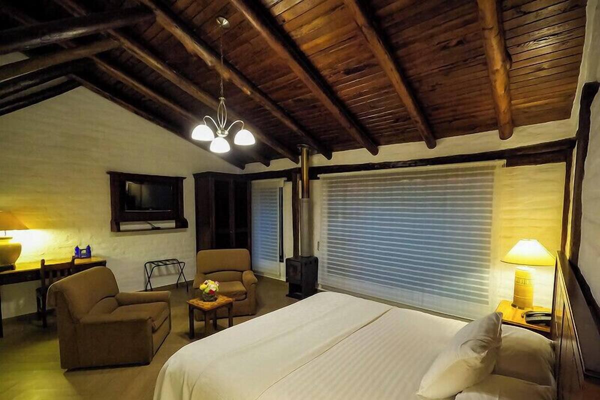A bedroom with a bed, two armchairs, a small table, a television, and a window with blinds.